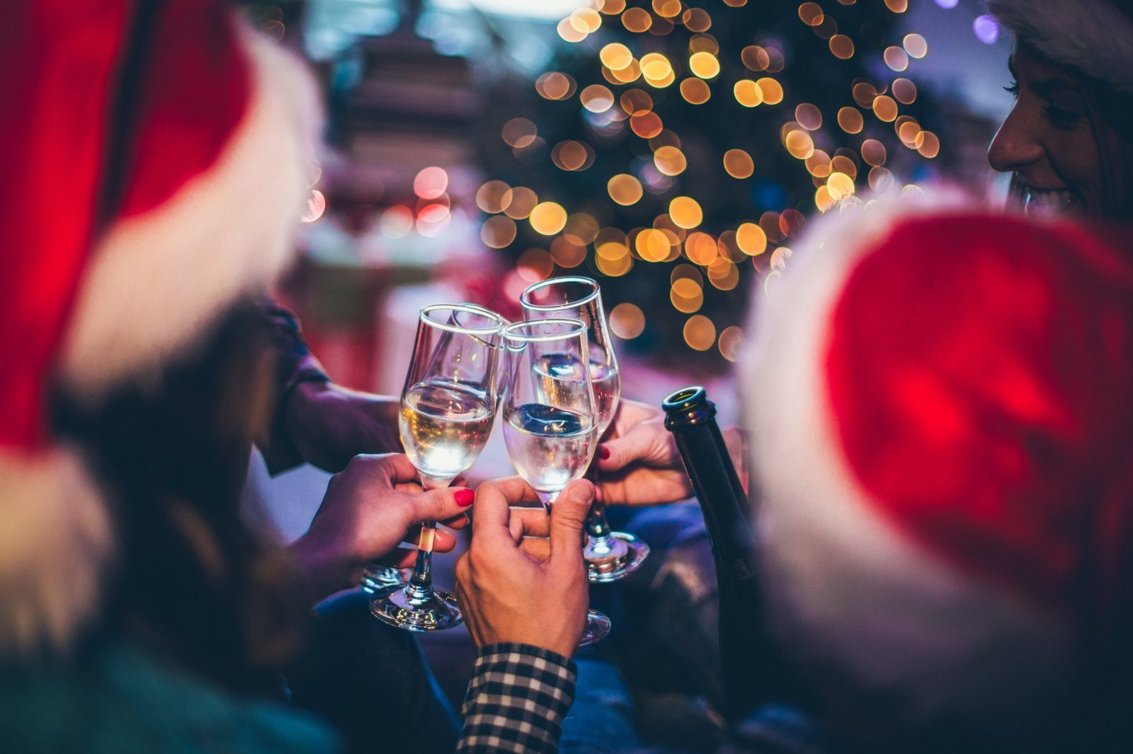 Anstoßen mit Sekt vor dem Weihnachtsbaum, Gäste mit Weihnachtsmützen